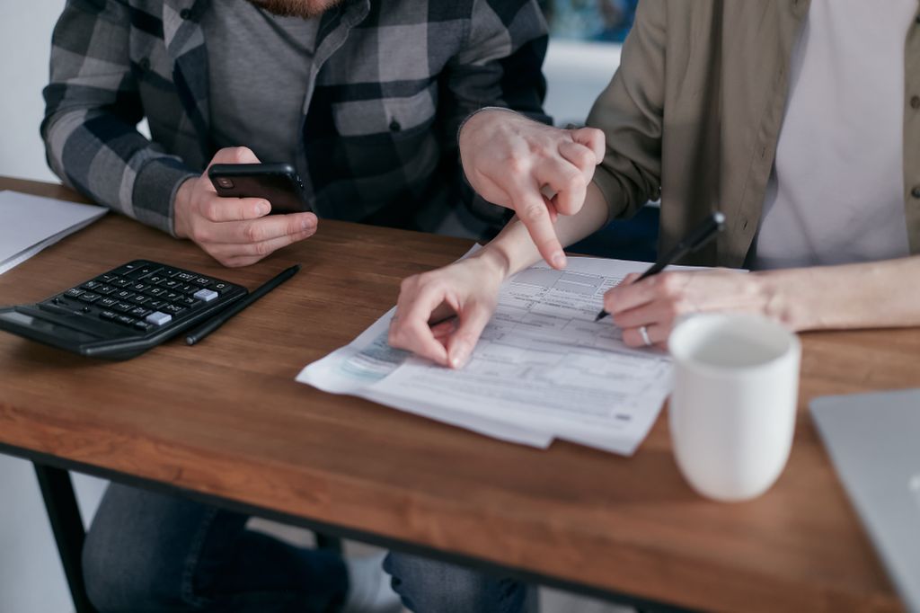 A couple at a kitchen table reviewing financial documents with a calculator