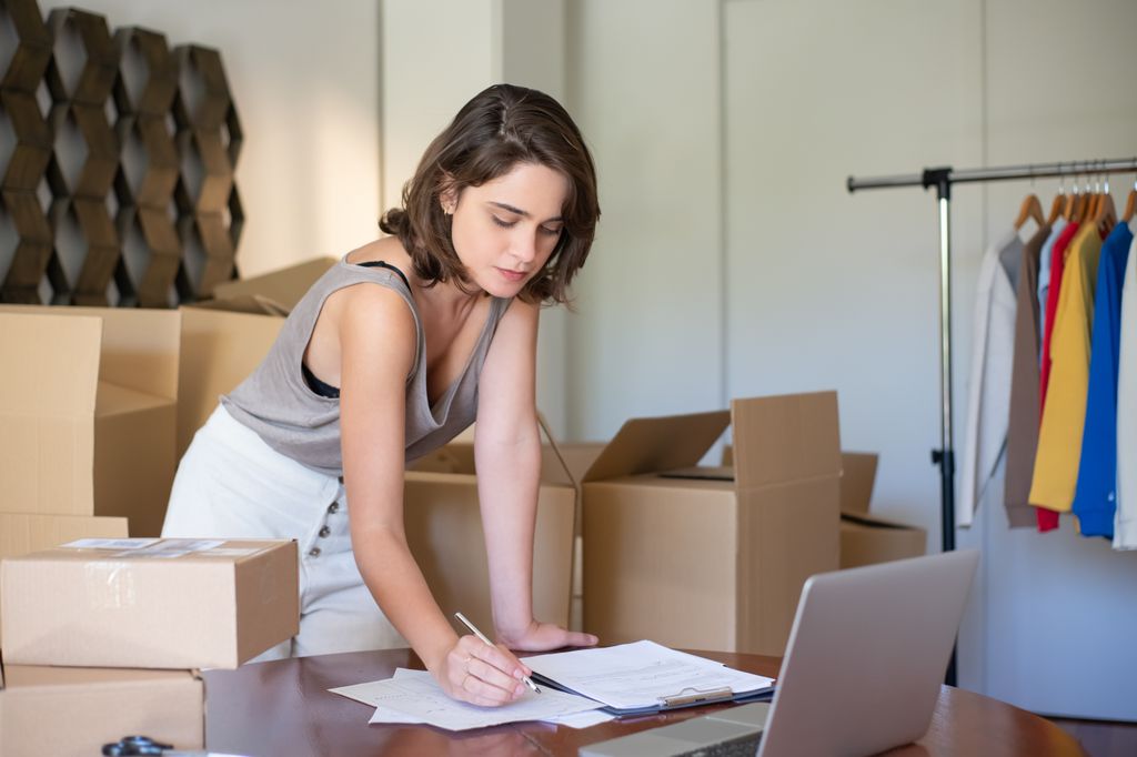 A small business owner working on paperwork at a desk beside shipping boxes